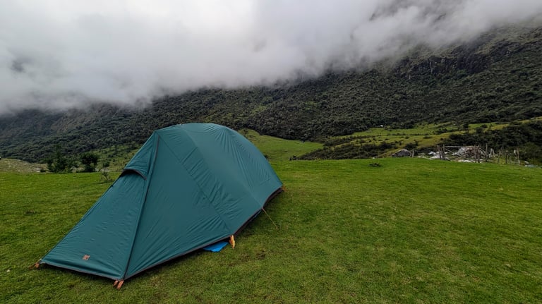 Blue tent pitched on green meadow with misty mountains and valley in background