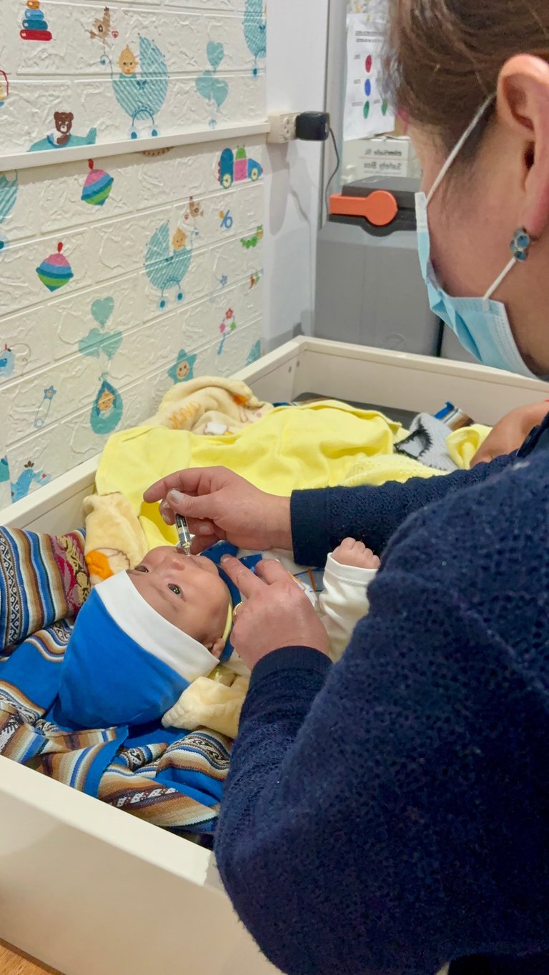 Healthcare provider examining infant in medical setting with colorful childrens drawings on wall behind