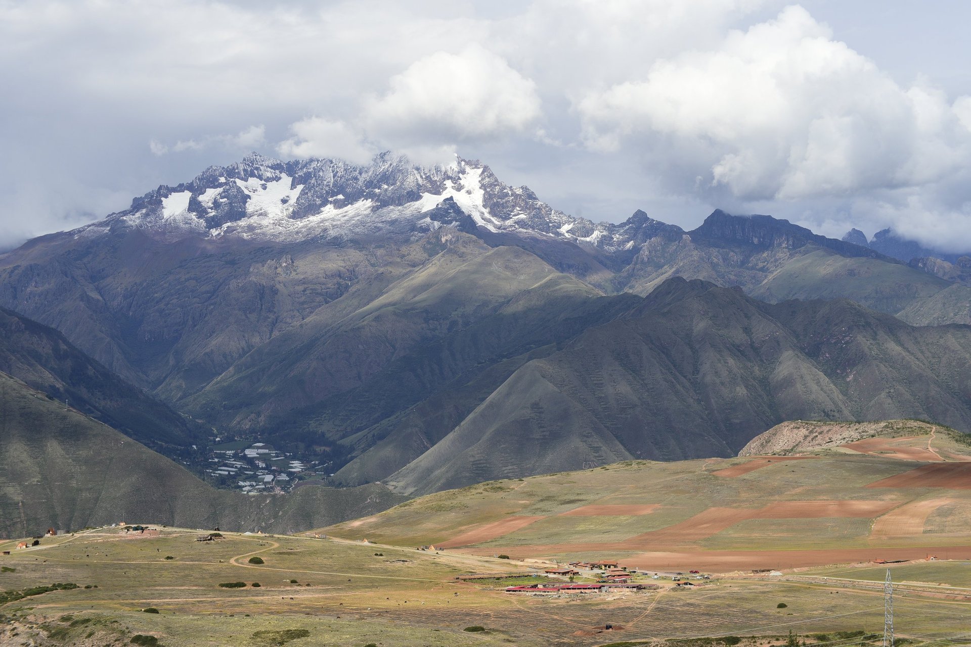 Snow-capped mountain peak rises above a high-altitude valley with agricultural fields and scattered settlements below
