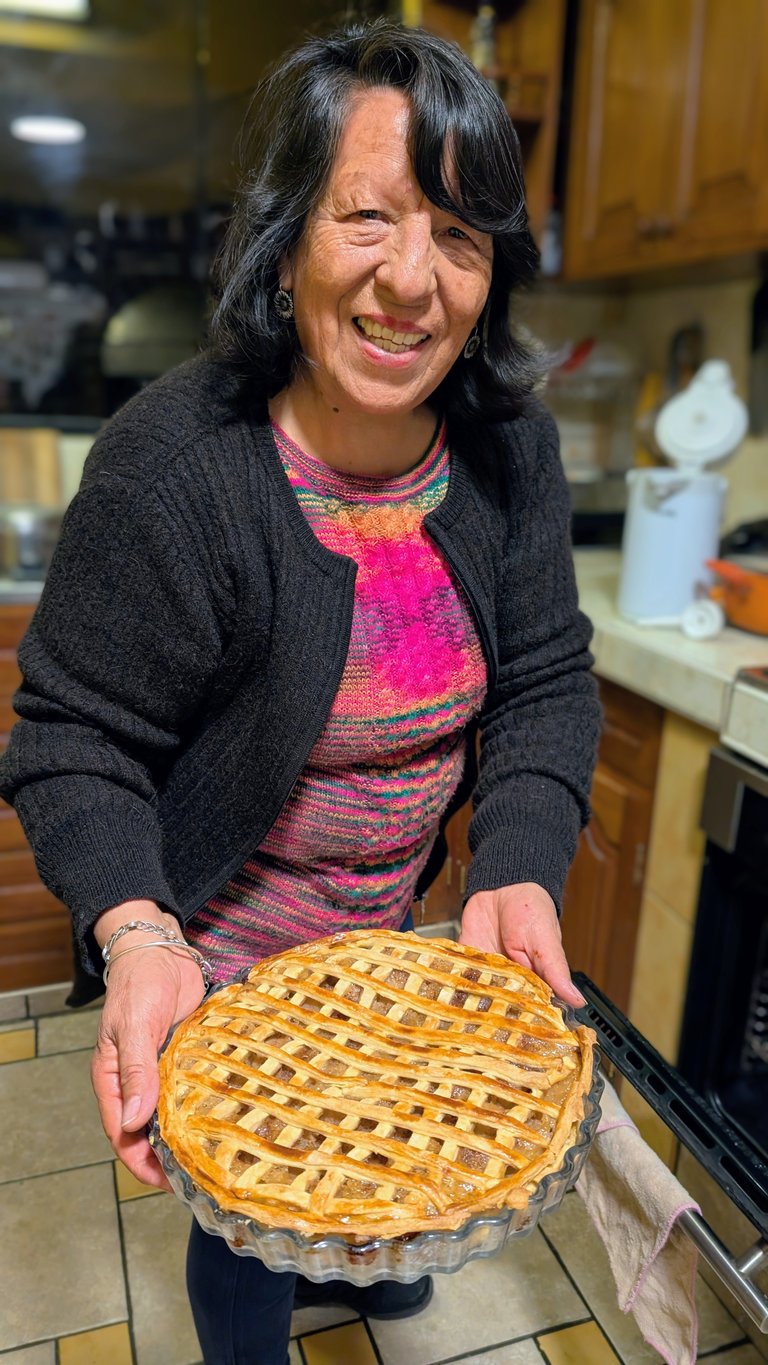 Woman smiling in kitchen holding a freshly baked fruit pie with lattice crust