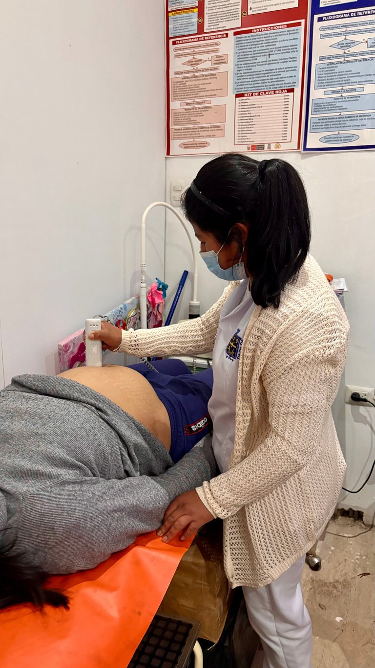 Healthcare worker in white coat and mask performing ultrasound examination on patients abdomen in clinical setting