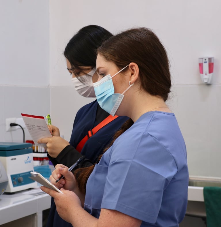 Two healthcare workers wearing surgical masks and PPE examining a medical chart in a clinical setting