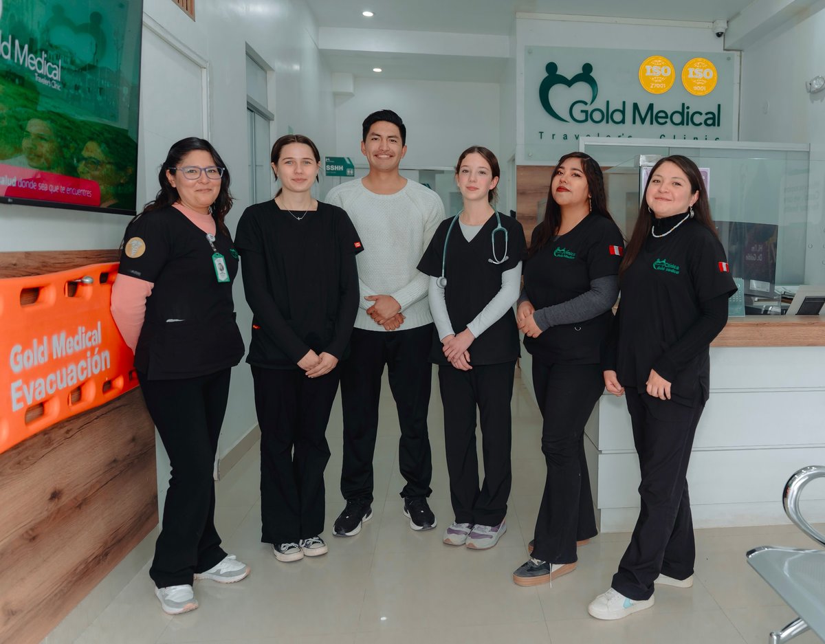 Six healthcare team members posing together in a medical clinic reception area with Gold Medical branding visible