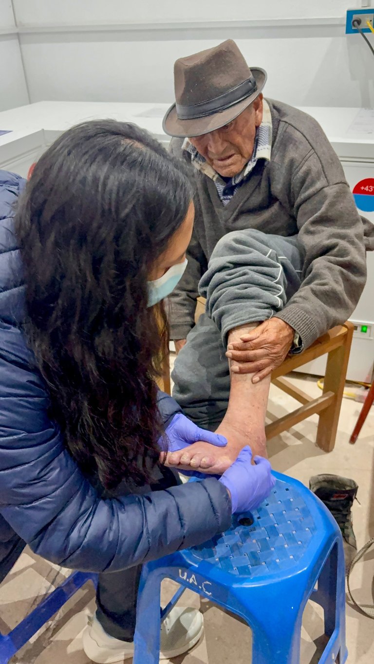 Healthcare worker in purple gloves examining the arm of an elderly man wearing a brown hat in a medical clinic setting