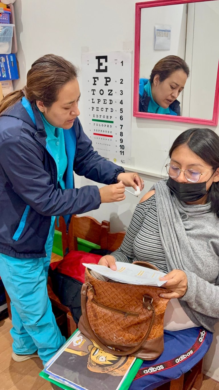 Healthcare worker showing a document to a young patient wearing glasses in a medical clinic setting with an eye chart visible on the wall