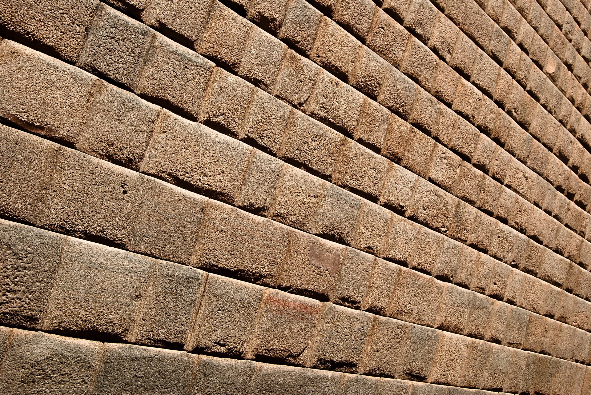 Angled view of rectangular tan and brown stone blocks arranged in diagonal rows with deep shadows between them