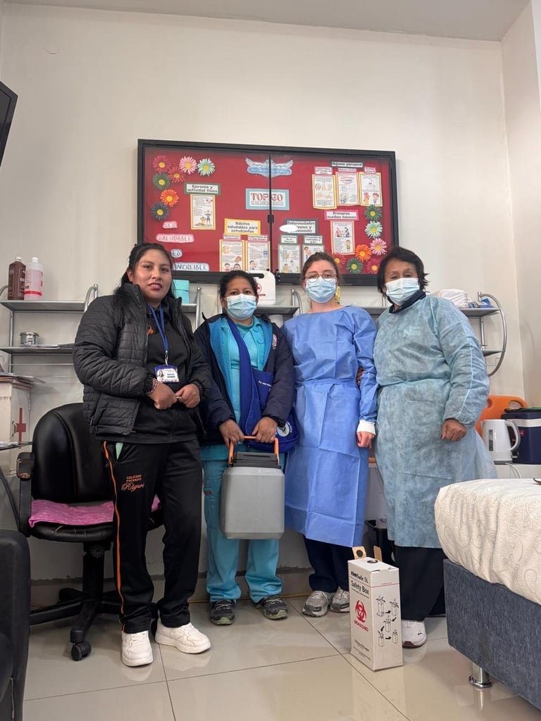 Four healthcare workers posing together in a medical office, three wearing face masks and medical scrubs, standing in front of a bulletin board
