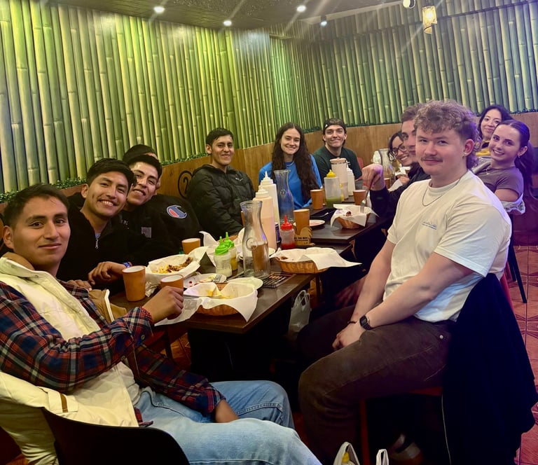 Group of people dining together at a restaurant table, smiling at the camera with food and drinks